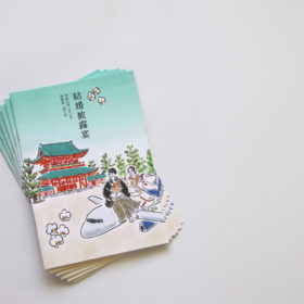 平安神宮外観と飛行機の上に乗っている新郎新婦のイラストが描かれた冊子の表紙